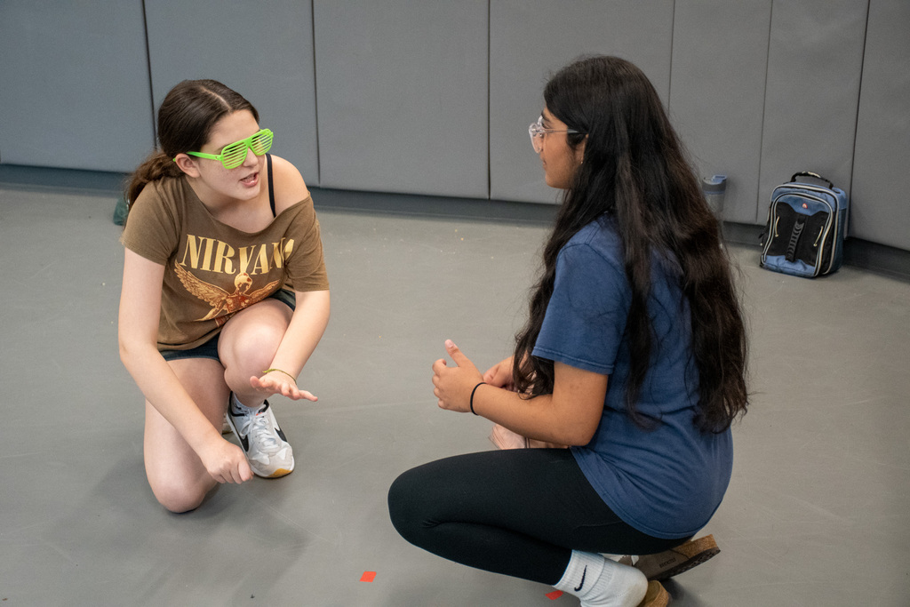 two student crouch on floor talking to each other during rehearsal at theatre workshop