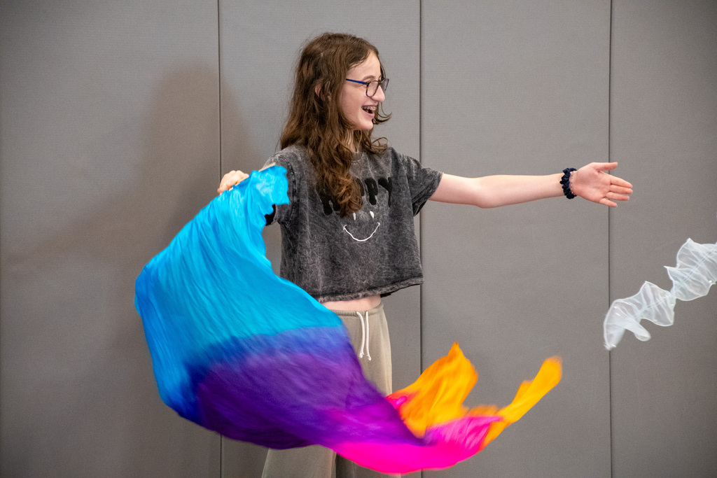 student waves multi-colored cloth banner in the air during skit at theater workshop