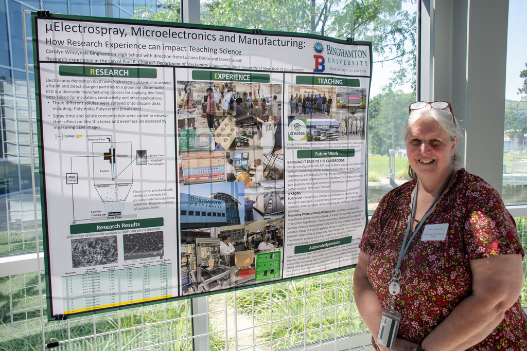 bhs teacher carolyn wilczynski stands next to a poster inside the binghamton university ITC rotunda