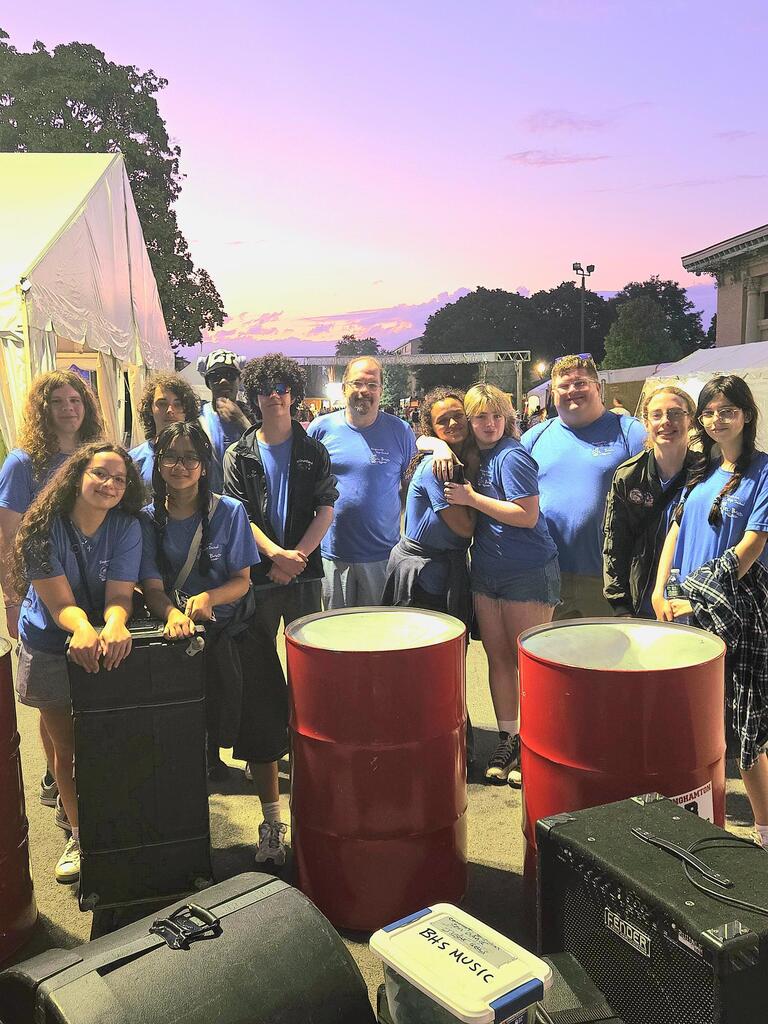 juice blenders steel drum band poses for photo with their drums at nys fair with sunset in background