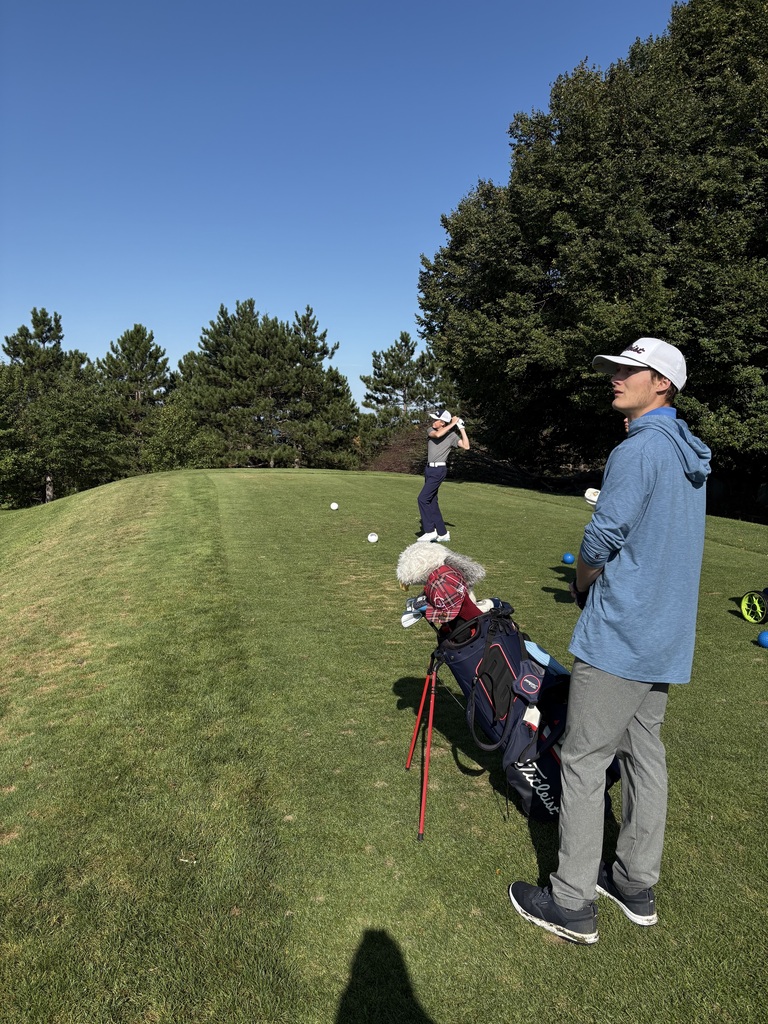binghamton golfer stands in follow through position after hitting a ball at the driving range while teammate looks on