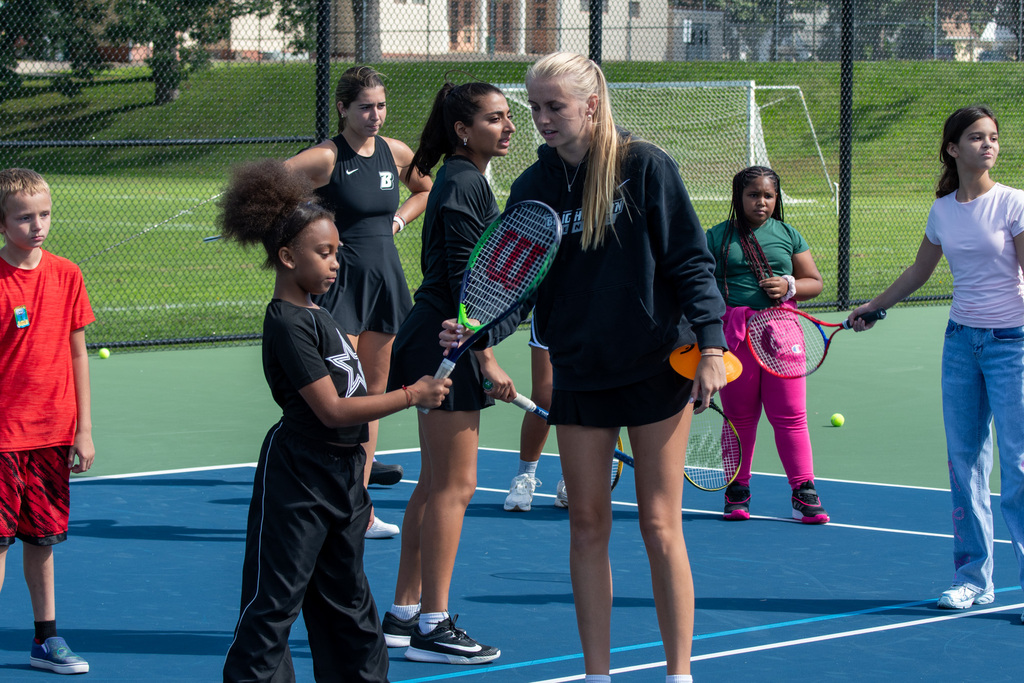 binghamton university women's tennis player shows horace mann student how to hold racket