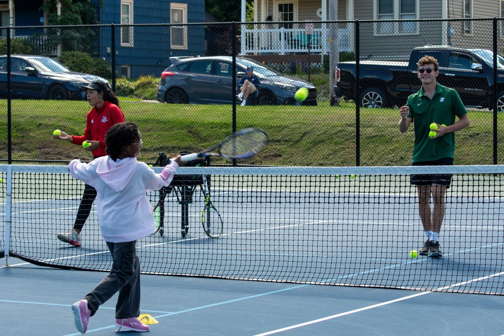 binghamton university men's tennis player tosses tennis ball to horace mann student who swings racket