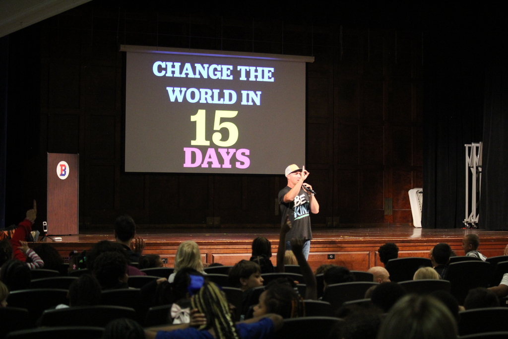 guest speaker addresses students in Ben Franklin auditorium with image behind him that says "Change the World in 15 Days"