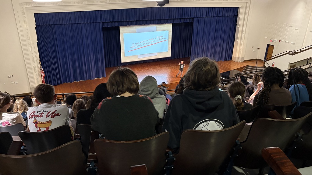 students sit in balcony of west middle school auditorium while listening to "Think Kindness" presenter Brian Williams speaking on stage
