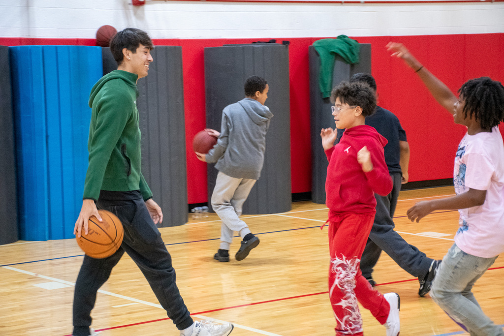 binghamton university men's basketball player dribbles ball while playing one on one with east middle student