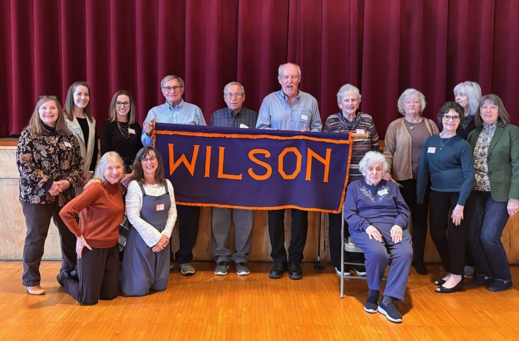 memers of woodrow wilson alumni association and current principal and assistant principal pose for photo holding banner that says "wilson"