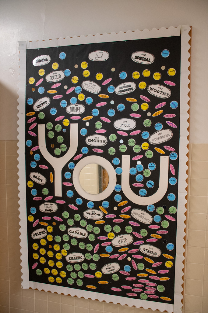 poster in hallway with small stickers that have positive adjectives typed on them; in the middle is a large print out of the word "you"