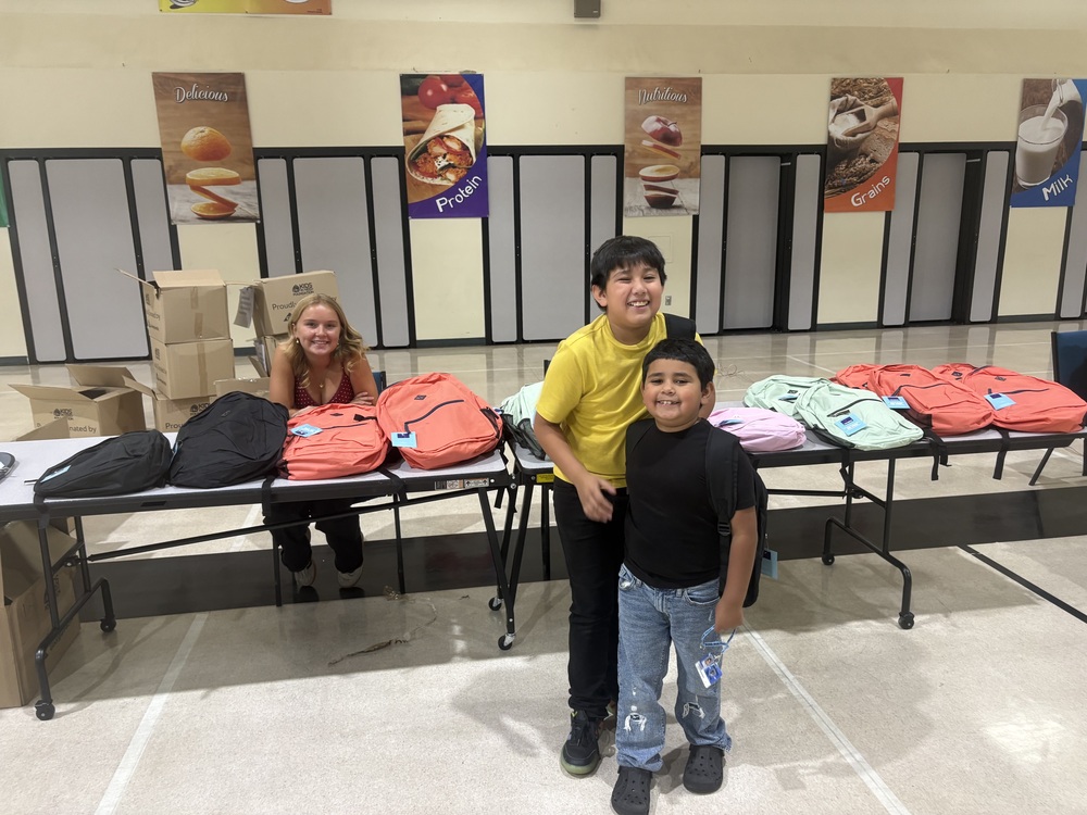 Students smiling with free backpacks filled with school supplies.