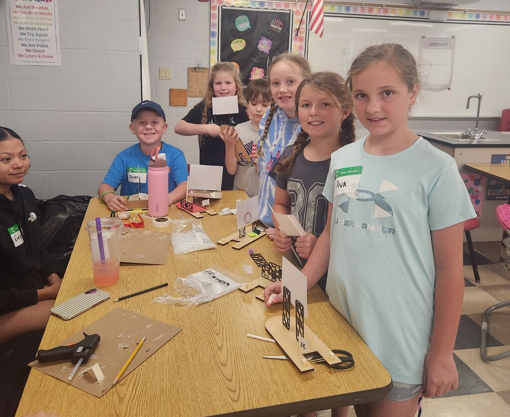 Boys and girls stand around a table in front of their Camp Invention projects