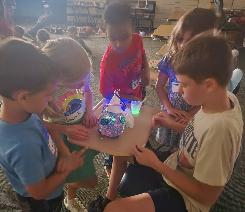 Boys and girls gather around a student working on a project during Camp Invention