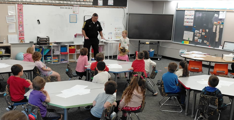 A fireman brings a young boy up to the front of the class to demonstrate a fire safety lesson in front of the class
