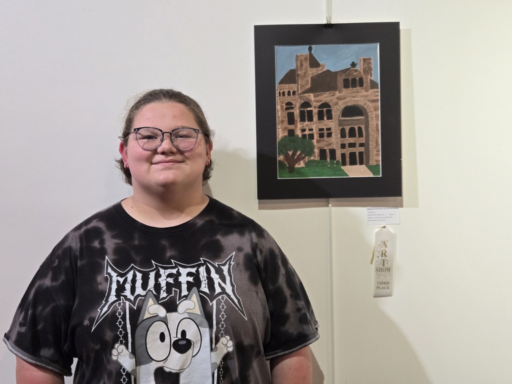 Ella Whetzel stands alongside her painting "Court House" as part of the Plein Air Paint Out on the Square exhibition