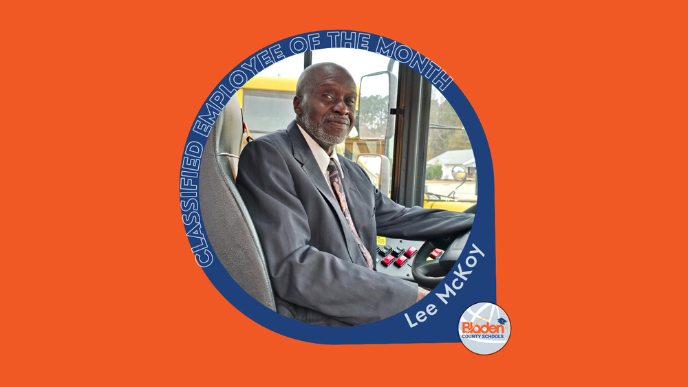 ELee McKoy, Classified Employee of the Month, seated in the driver’s seat of a school bus, smiling at the camera.