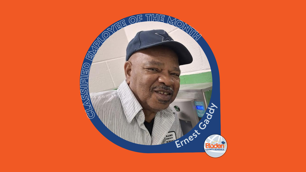 Portrait of Ernest Gaddy, Classified Employee of the Month for Bladen County Schools, wearing a striped work shirt and baseball cap, smiling indoors near equipment.