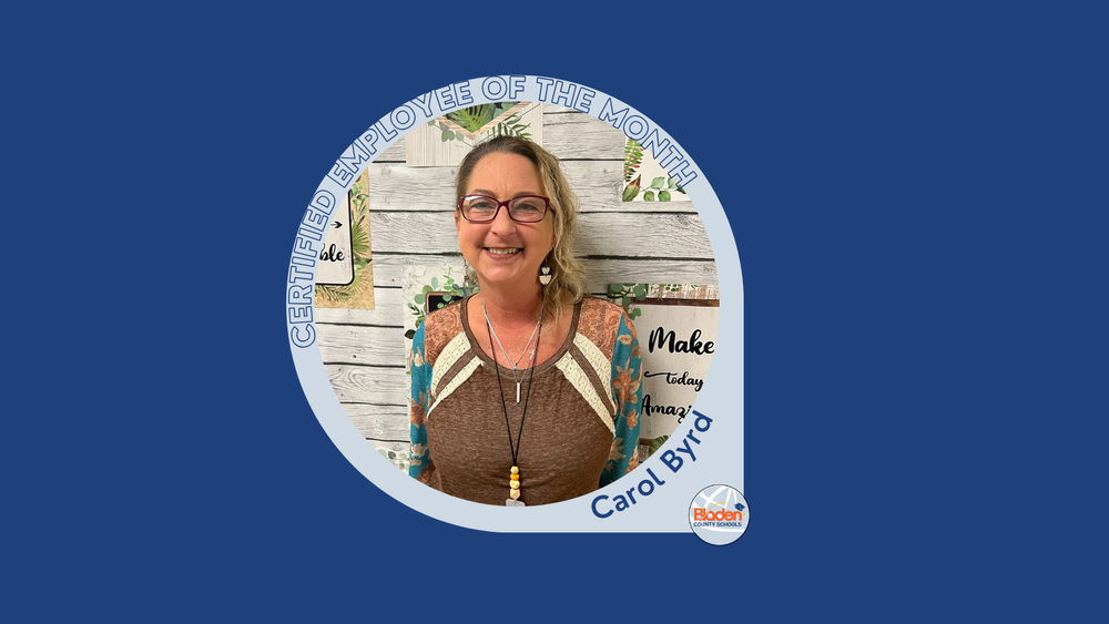 Carol Byrd, Certified Employee of the Month, smiling indoors in front of a decorative classroom backdrop.