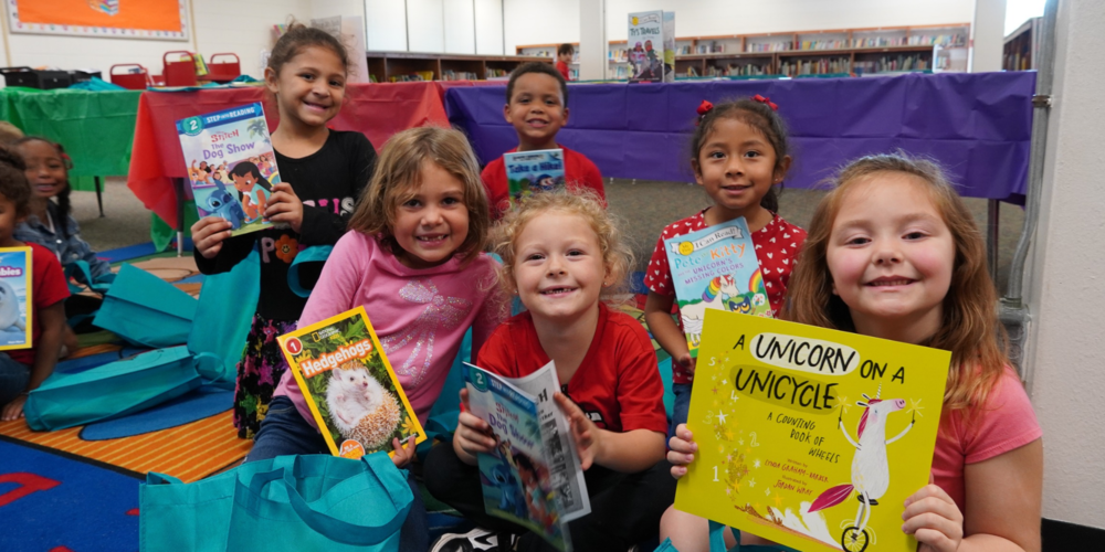 A group of kindergarten students smiling with new books.