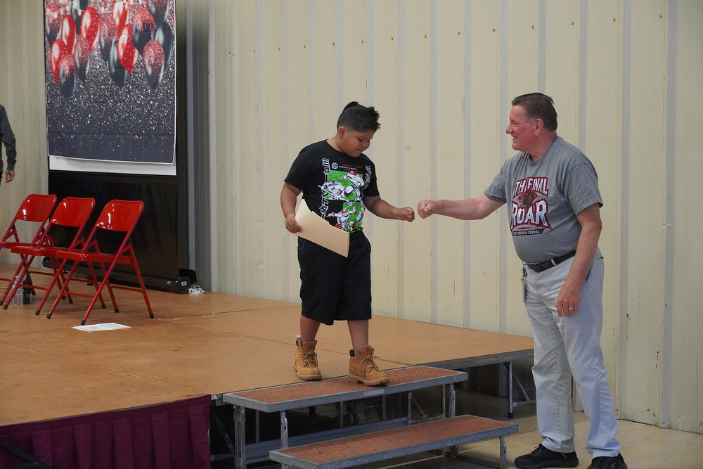 A student walking off a stage is giving a celebratory fist bump to the school principal.