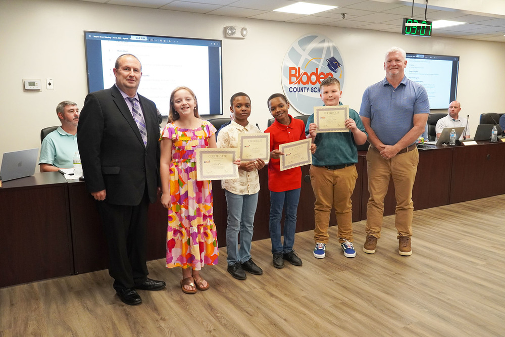 elementary students holding certificates standing between two adults
