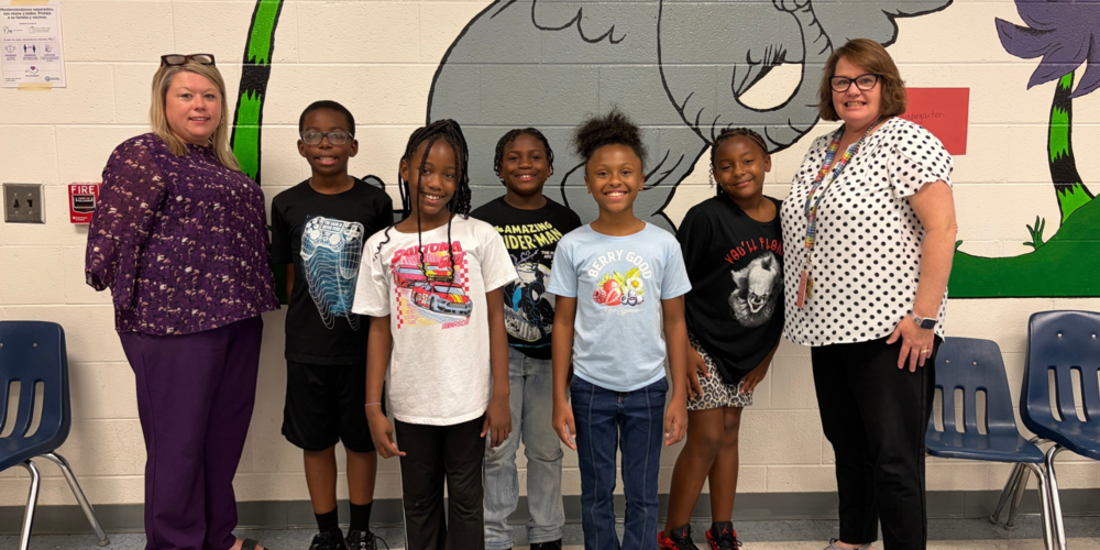 Elizabethtown Primary's Principal and Media Coordinator pose in front of a mural with 5 students.