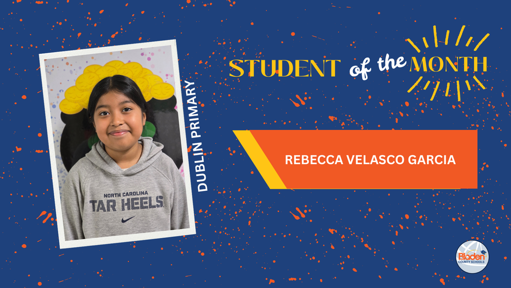 Student of the Month graphic featuring Rebecca Velasco Garcia from Dublin Primary, smiling while standing in front of a colorful classroom mural, wearing a gray Tar Heels hoodie, with bold blue and orange design elements and Bladen County Schools logo.