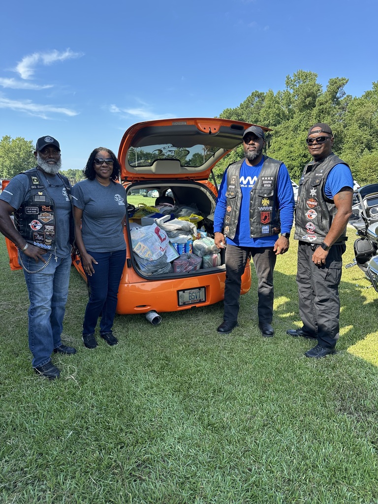 Members of Big Swins standing beside orange car with trunk open and full of school supplies