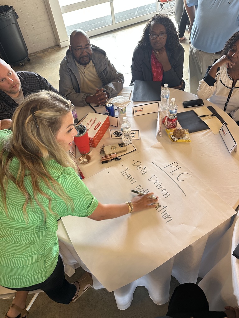 Tar Heel team writing “PLC = Data Driven, Team Collaboration” on chart paper during discussion.