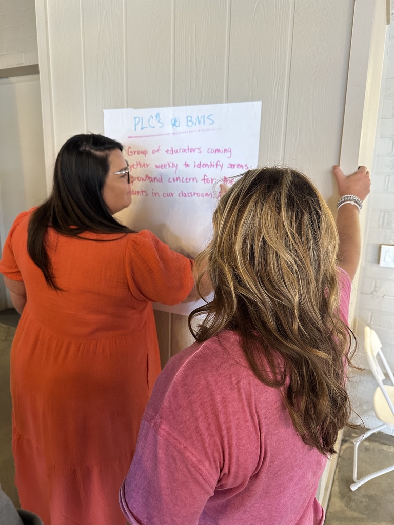 Two educators from Bladenboro Middle School posting their PLC definition on the wall.