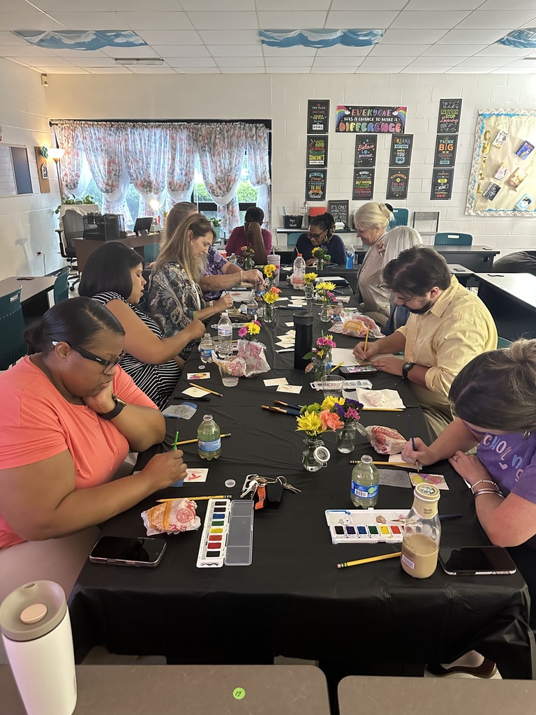 Group of adults sitting at a long table painting together.