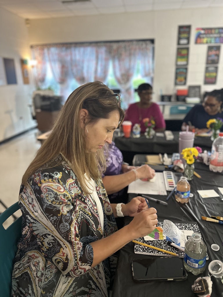 Woman painting with watercolors on paper at a black-covered table.