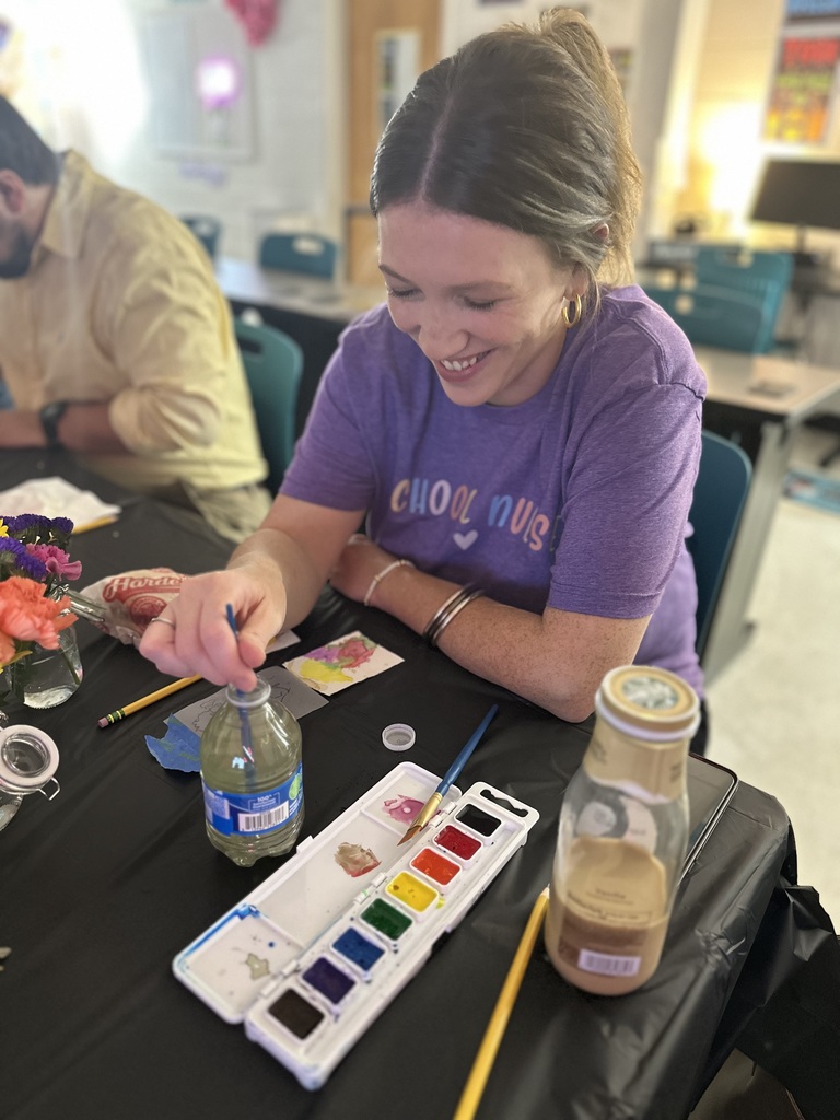 Woman smiling while painting with watercolors at a table.