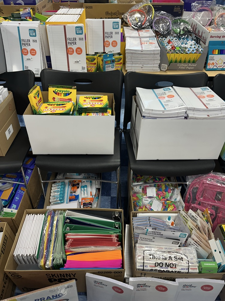 Stacks of filler paper, Crayola supplies, binders, glue sticks, and assorted school supplies in boxes.