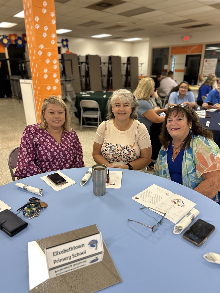 Three women sit at a blue table with an Elizabethtown Primary School sign in a cafeteria
