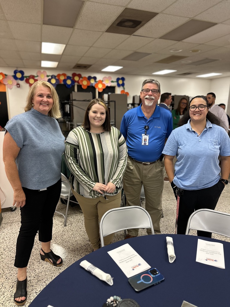 Four people stand together behind a blue table with folded napkins and programs