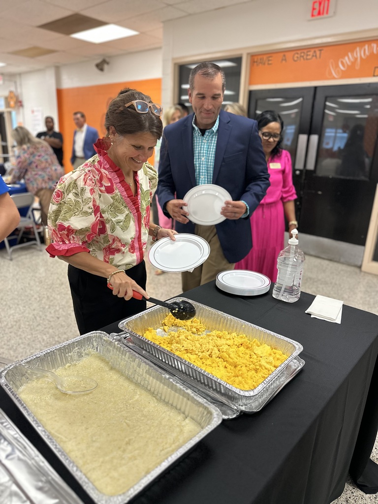 Woman serves scrambled eggs from buffet trays while others wait in line holding plates