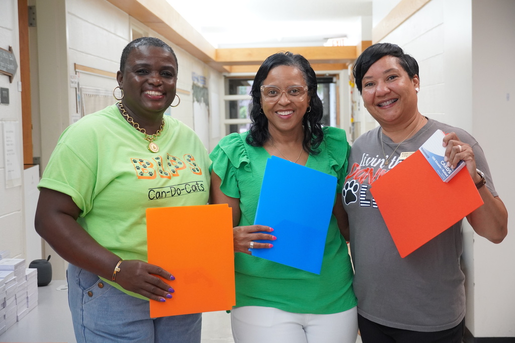 Three staff members holding folders and smiling in a school hallway