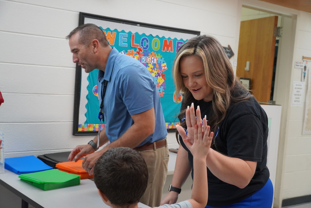 Staff member high-fives a student while handing out folders at school entrance.