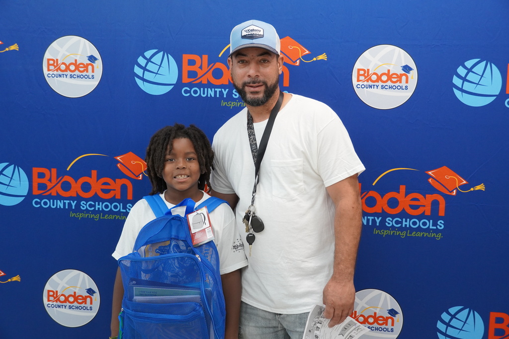 Student with backpack and parent smiling in front of Bladen County Schools backdrop