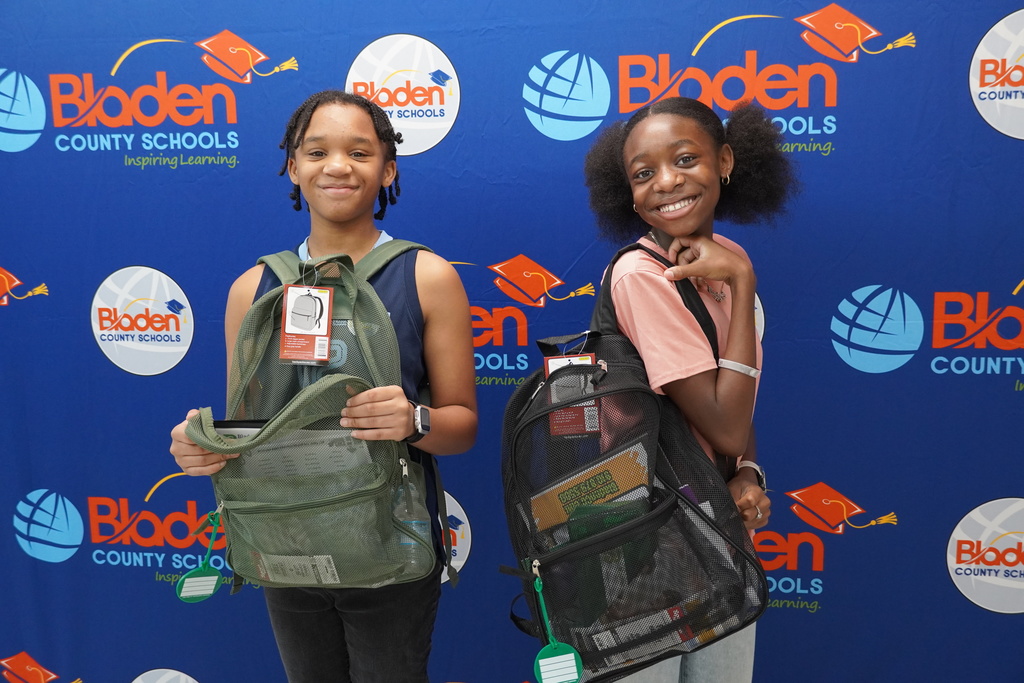 Two middle school students posing with clear backpacks in front of district backdrop