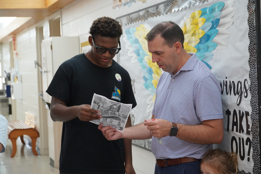 Student and staff member look at a paper together in school hallway