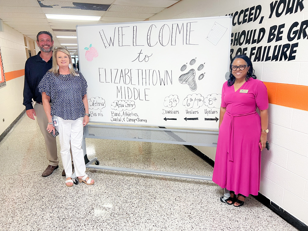 Three staff members stand beside a “Welcome to Elizabethtown Middle” sign in a hallway.