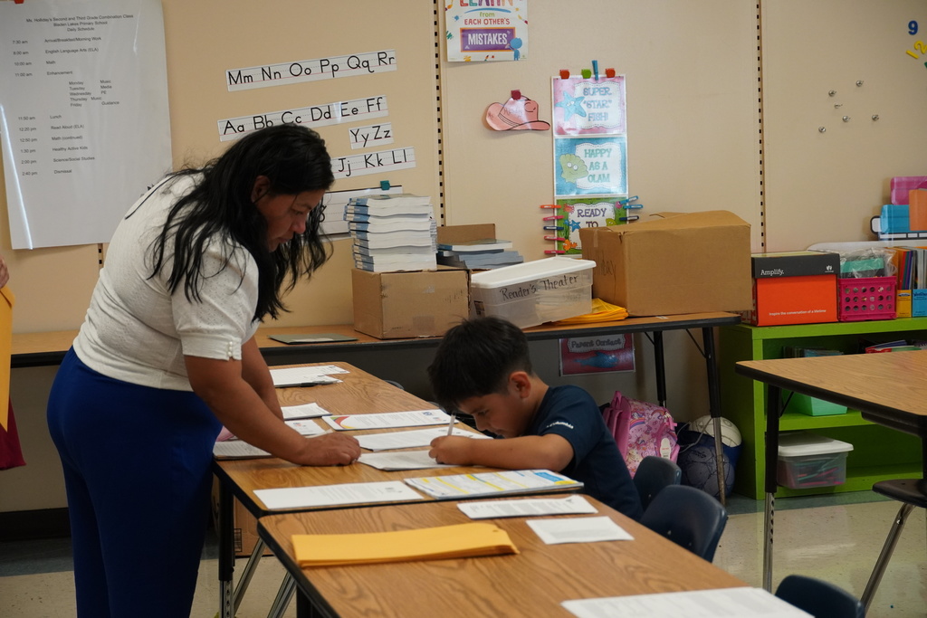 Parent helps child fill out paperwork at a classroom table during Open House.