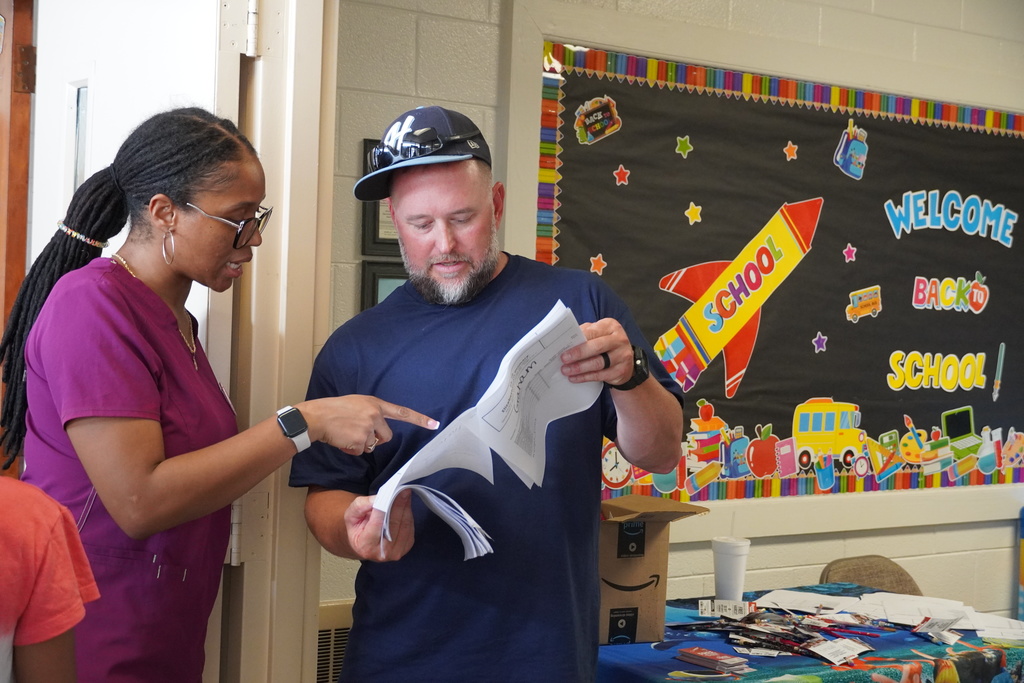 Staff member points out details on paperwork to a parent during Open House, near a back-to-school display.