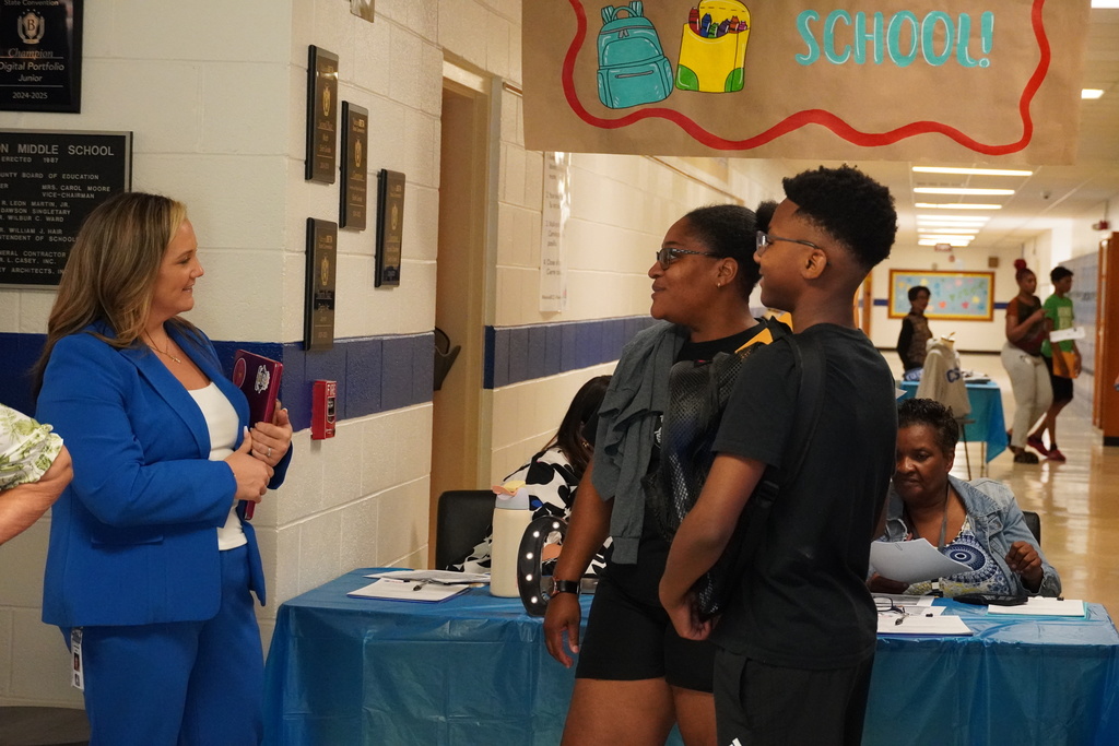 Administrator greets a student and parent under a “Welcome Back to School” banner.