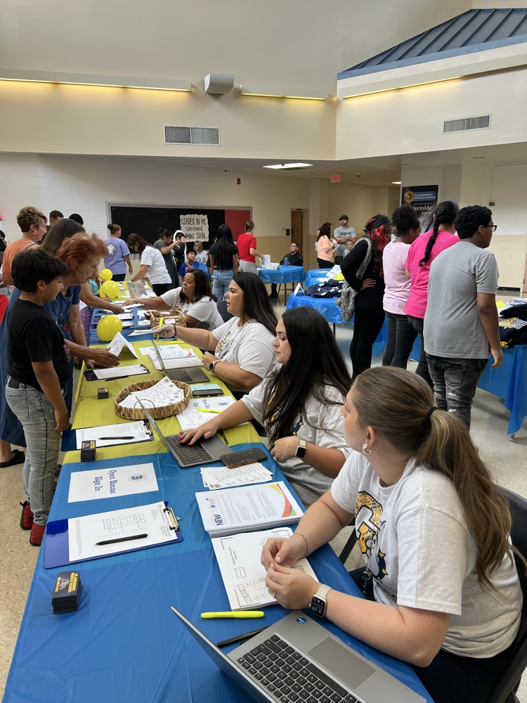adults sitting at a table checking students in at open house at a middle school