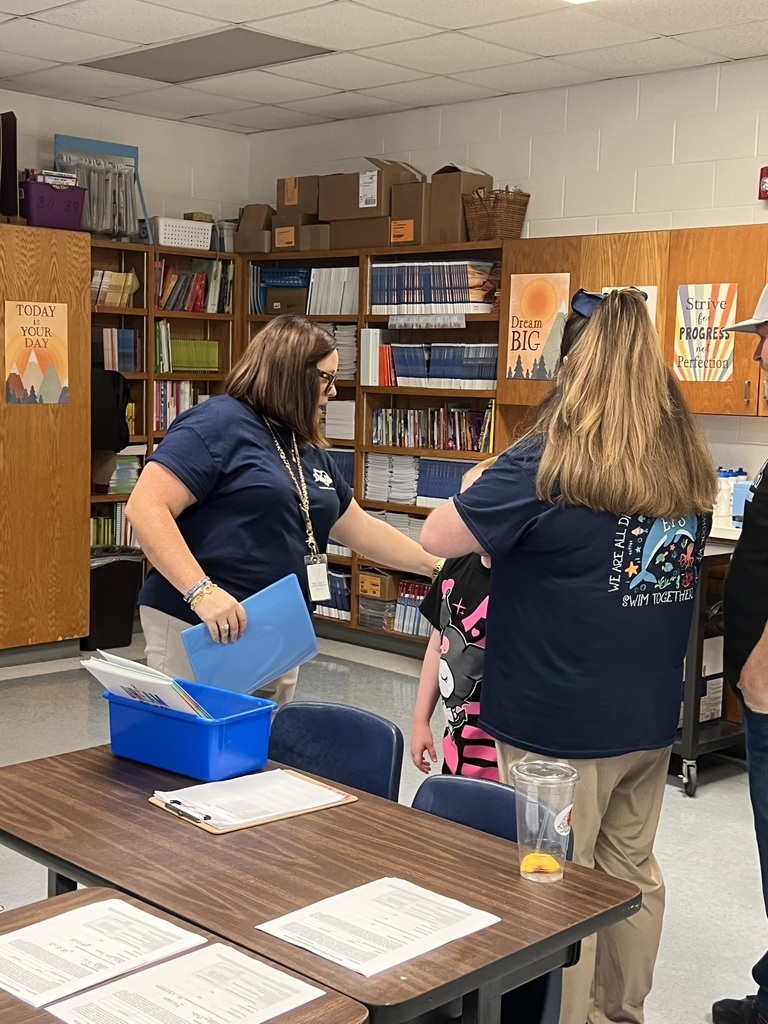 Teacher welcoming a student and family inside a classroom.