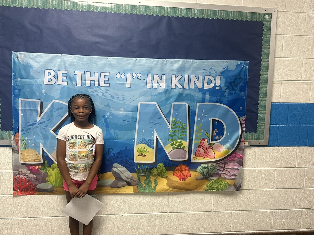 Student smiling while standing in front of a banner that says “Be the ‘I’ in Kind.”