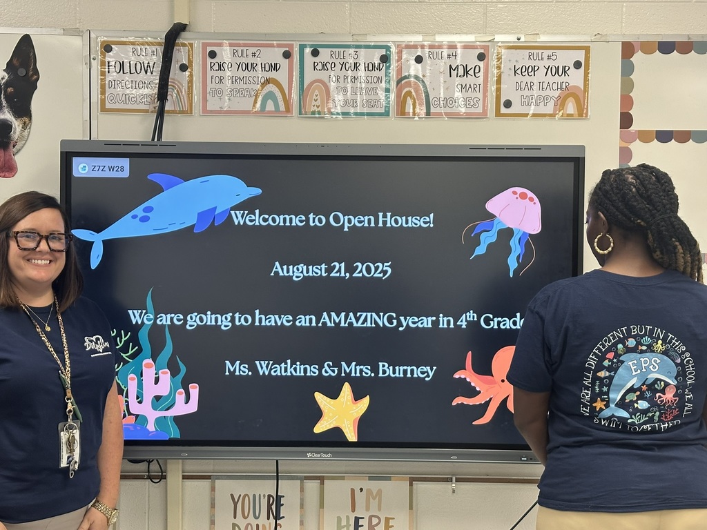 Two teachers standing by a classroom screen that reads “Welcome to Open House! August 21, 2025.
