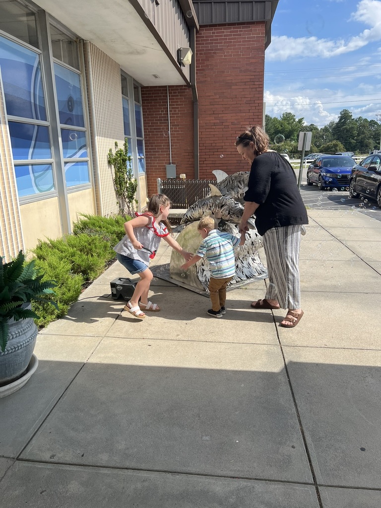 Children and a parent playing with bubbles outside the school entrance.