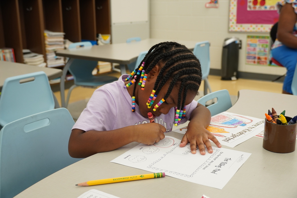 Young student colors worksheet at classroom table on the first day of school.